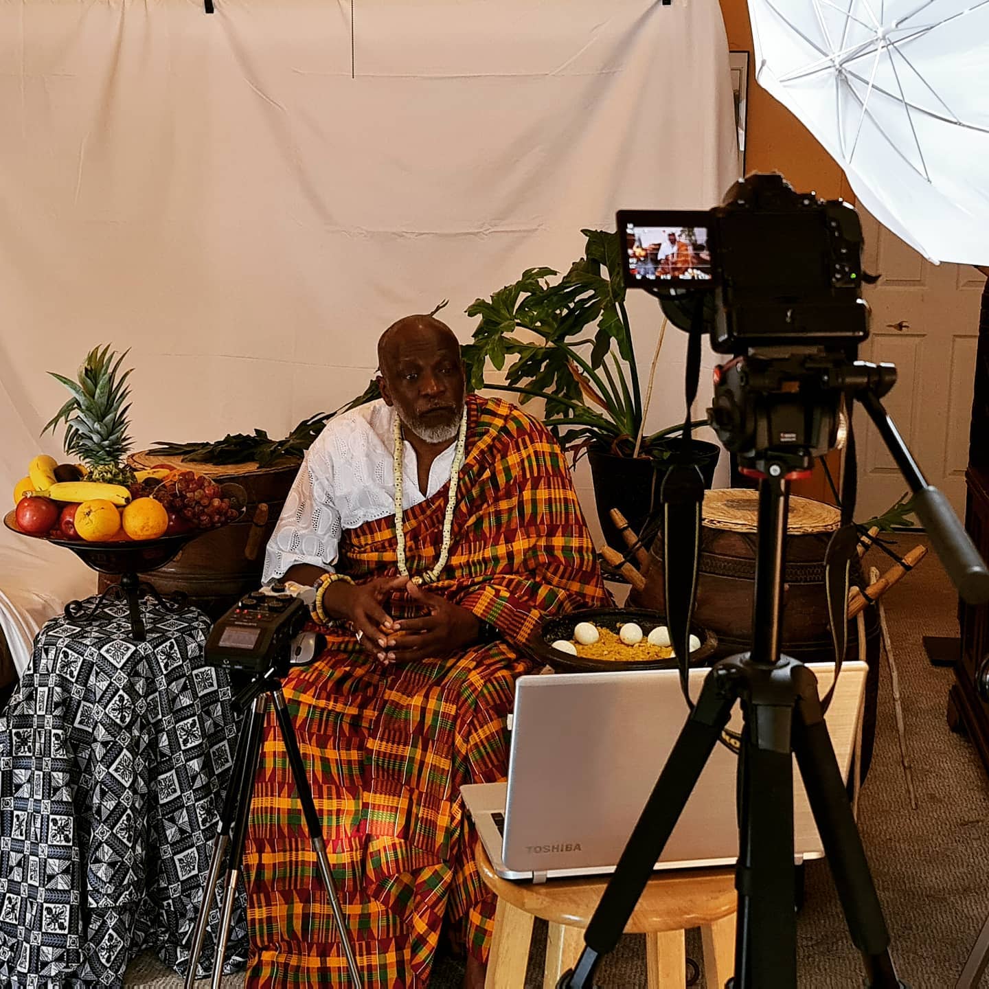 A seated participant in patterned cloth, with a camera and studio lights in the recording setup.